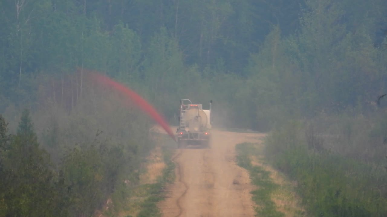 camión de bomberos conduciendo lentamente por un camino de tierra rociando retardante de fuego en incendios forestales canadienses