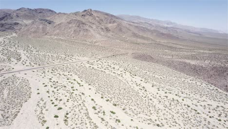 Drone-following-a-car-driving-in-the-distance-on-a-desert-road-in-4k