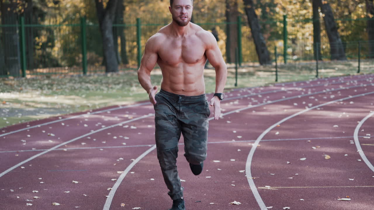 Fitness young man running at sports stadium. Shirtless sportsman running outside on athletics track in autumn. Healthy lifestyle.