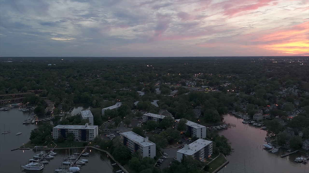 Nautilus Point Apartments in Annapolis, MD in der Dämmerung, während Boote ruhig auf glattem Wasser unter sanftem, farbenfrohem Himmel liegen – Drohnenflug vorwärts