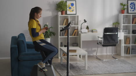 una deportista está chateando en redes sociales por teléfono celular durante el entrenamiento con una bicicleta estacionaria en la sala de estar en el descanso de fitness en el entrenamiento