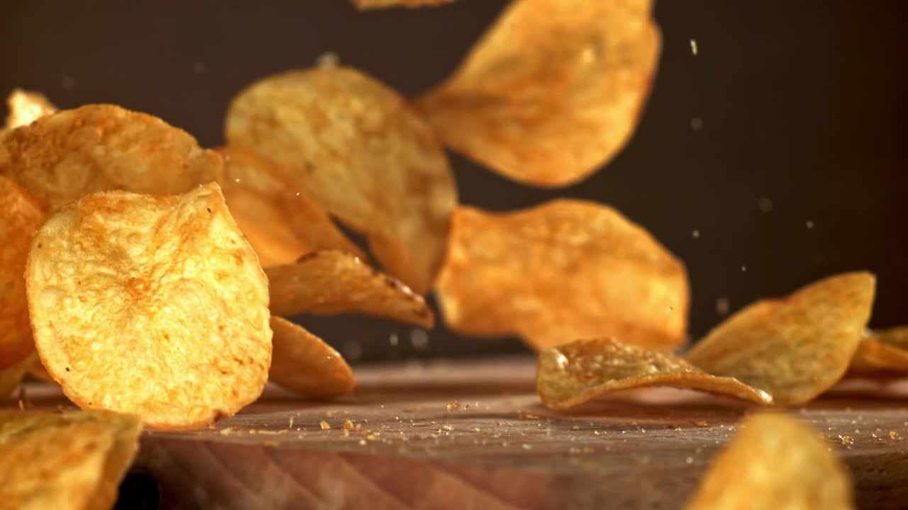 Crispy Potato Chips Dropping onto a Wooden Surface in Super Slow Motion
