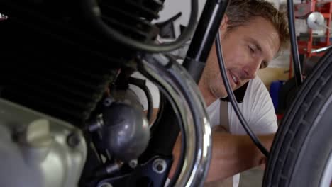 male mechanic talking on mobile phone while repairing motorbike in garage 4k