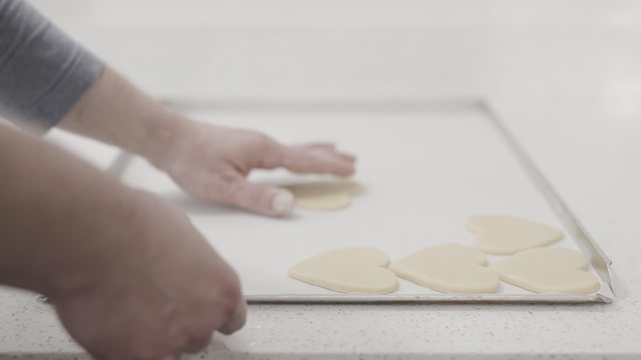 A steady shot of a man arranging freshly rolled out heart shaped butter cookies on a baking tray in a pastry shop, 4K
