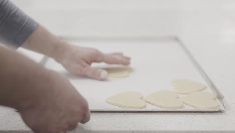 a steady shot of a man arranging freshly rolled out heart shaped butter cookies on a baking tray in a pastry shop, 4k