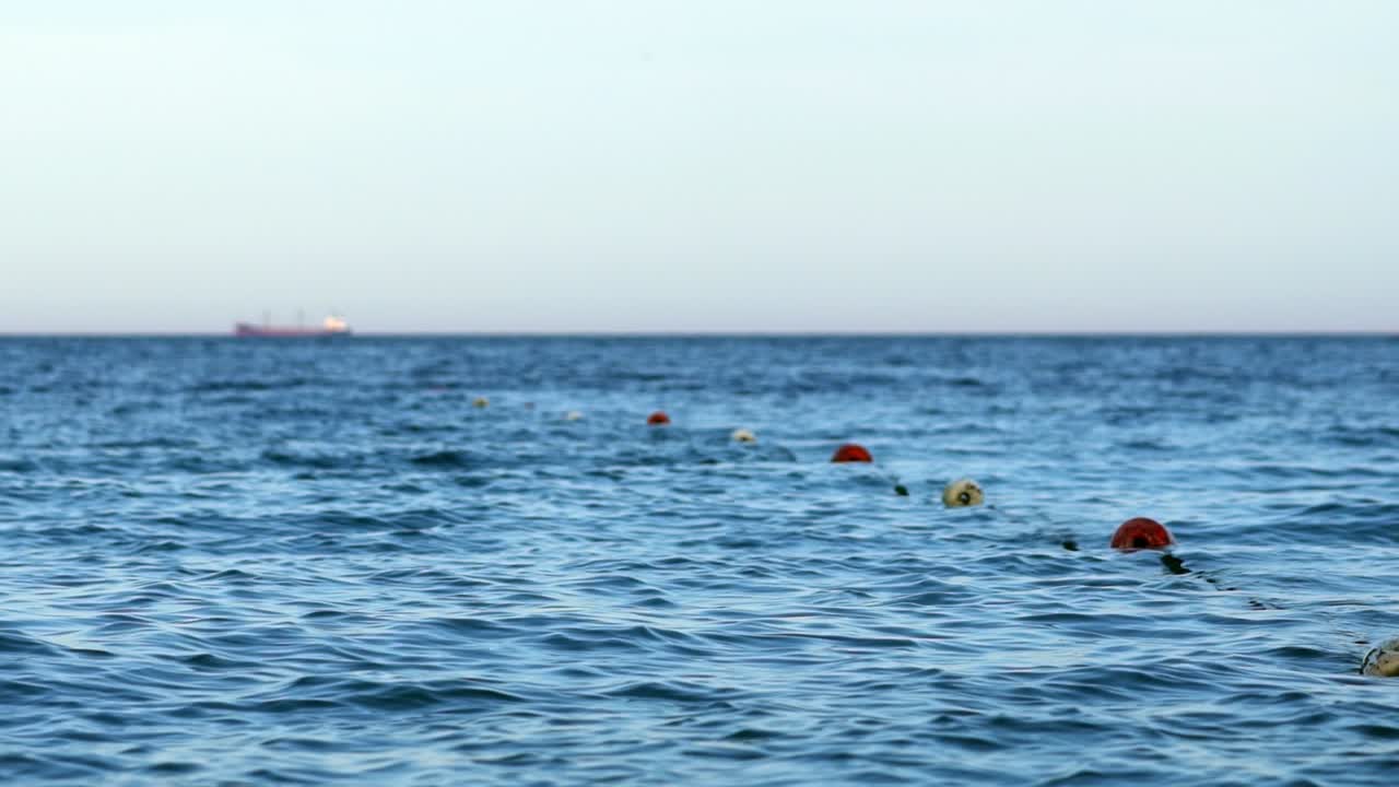 Floating fence of swimming area in sea marked with buoys. Marker area with buoys on blue water. Swimming zone border signs.