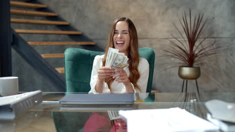 Joyful-business-woman-counting-money-in-office.-Girl-holding-wad-of-money.