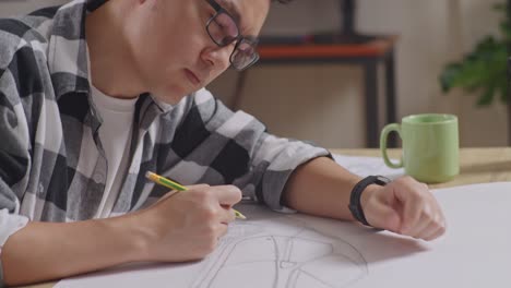 close up of asian male thinking about new car concept while working on a car design sketch on table in the studio