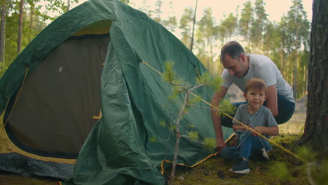 father and son together set up a tent in the woods during the summer campaign. father and son put up a tent in the autumn