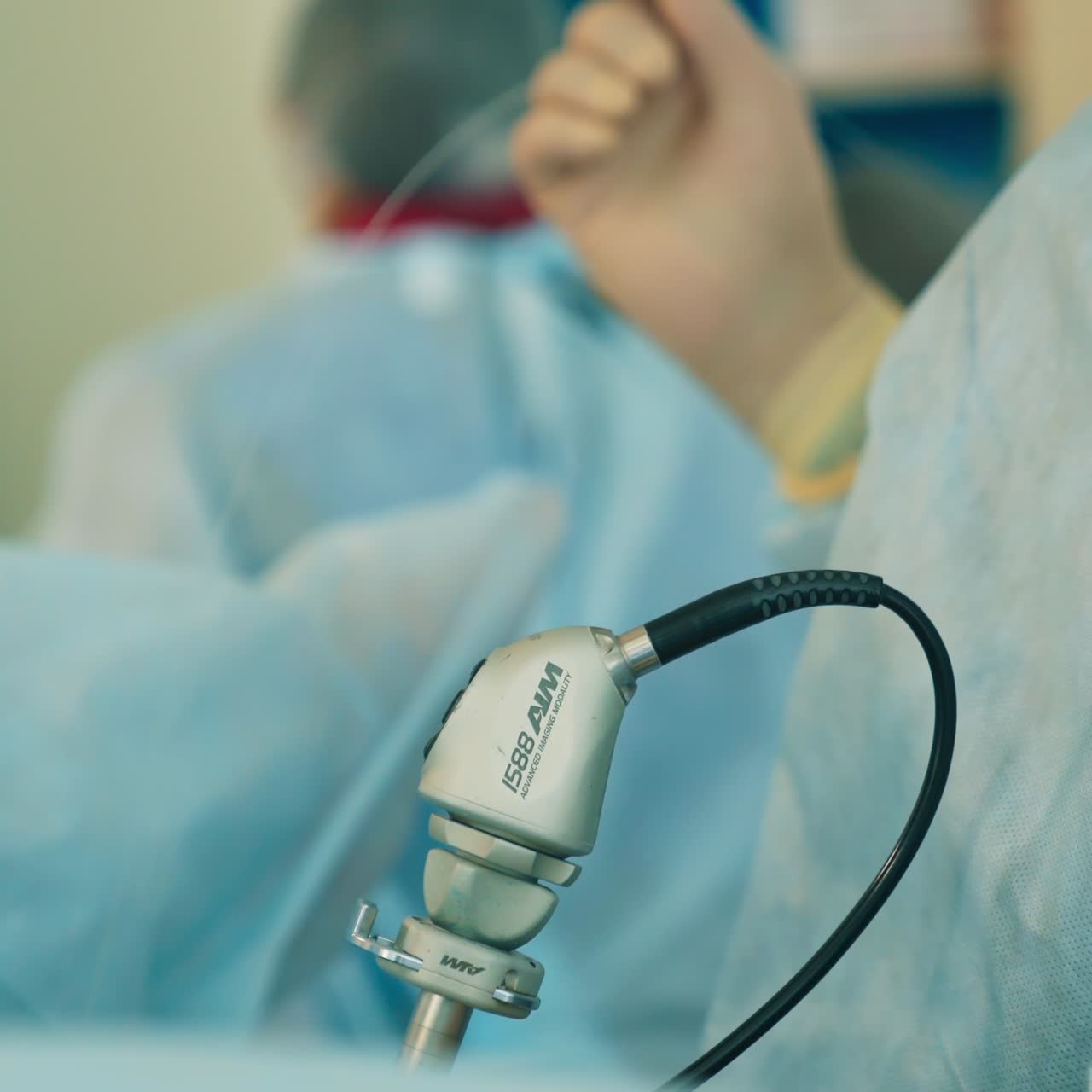 Surgeon's holds the instrument with one hand and pulls the wire by the other one. Medical staff moving at backdrop in blur