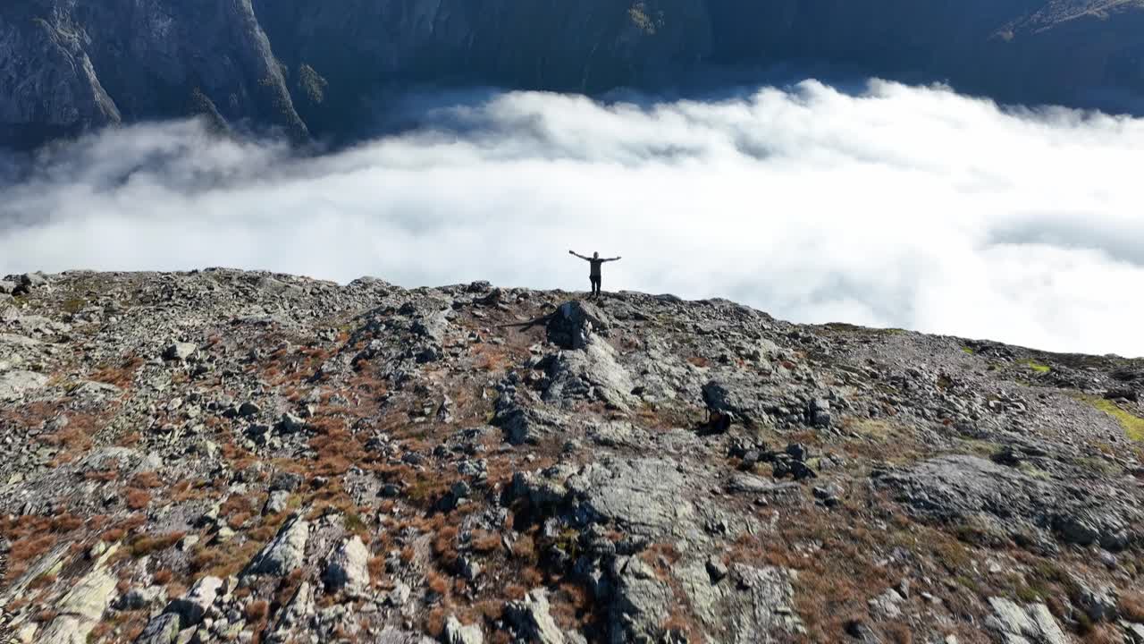 Drone flies forward close to the ground, then tilts up to reveal a man cheering on the edge of Bakkanosi, slowing down as the cheering begins