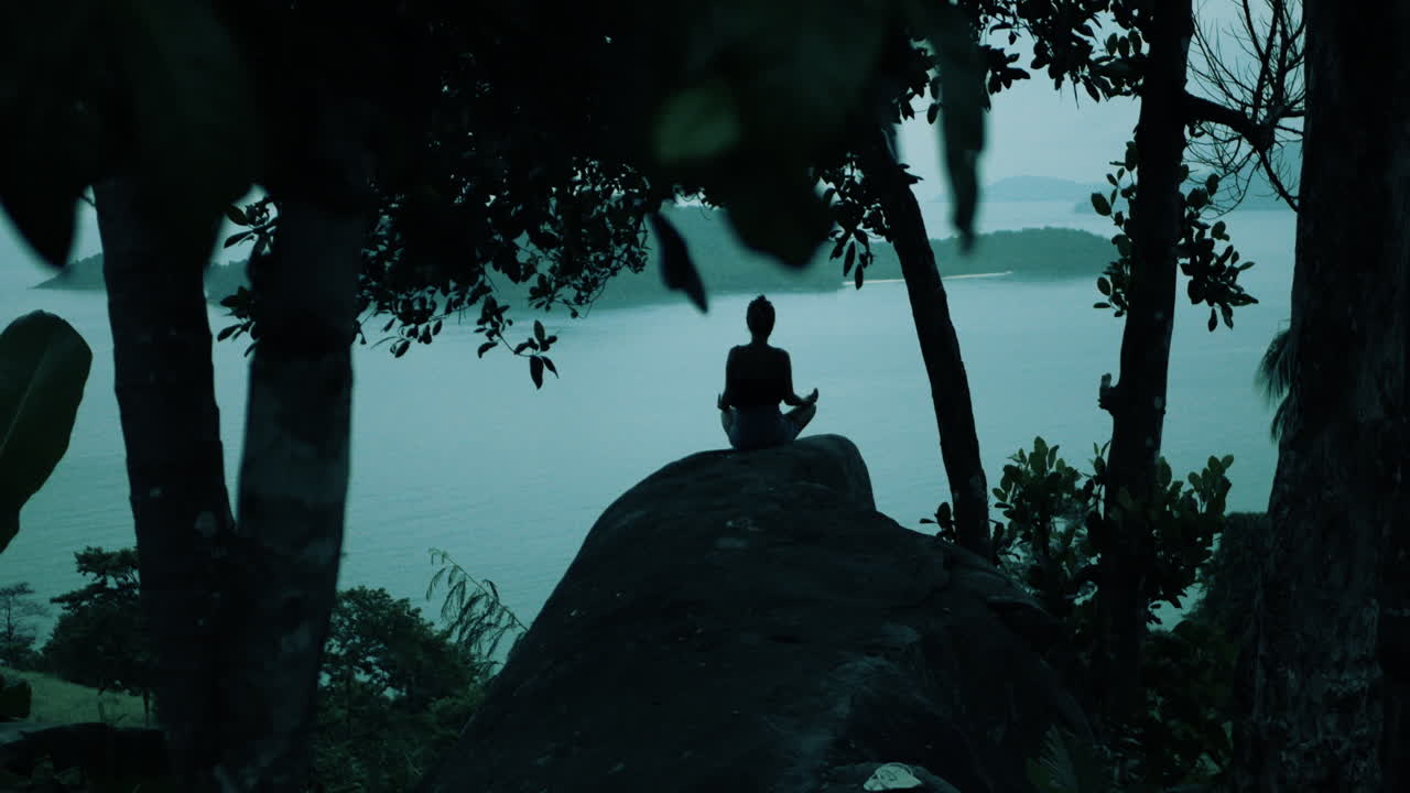 해가 지면 바다를 내려다보는 절벽에서 명상하는 여자