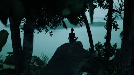 woman meditating on a cliff overlooking the ocean at sunset