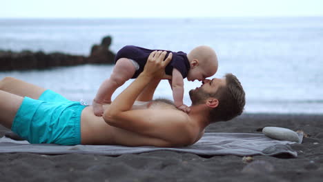 mientras está en la playa, un joven padre se involucra en momentos de juego con su hijo recién nacido. apreciando estos momentos de calidad, disfruta de sus vacaciones. es un padre contento y encantado