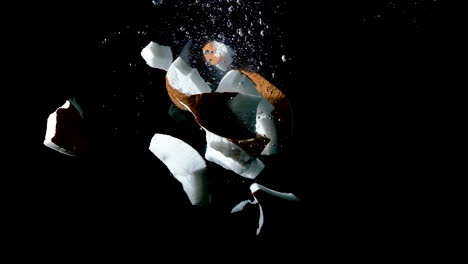 Smashed-coconut-shell-dropped-into-water-on-black-background,-slow-motion