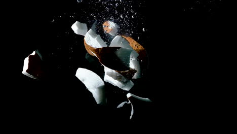 smashed coconut shell dropped into water on black background, slow motion