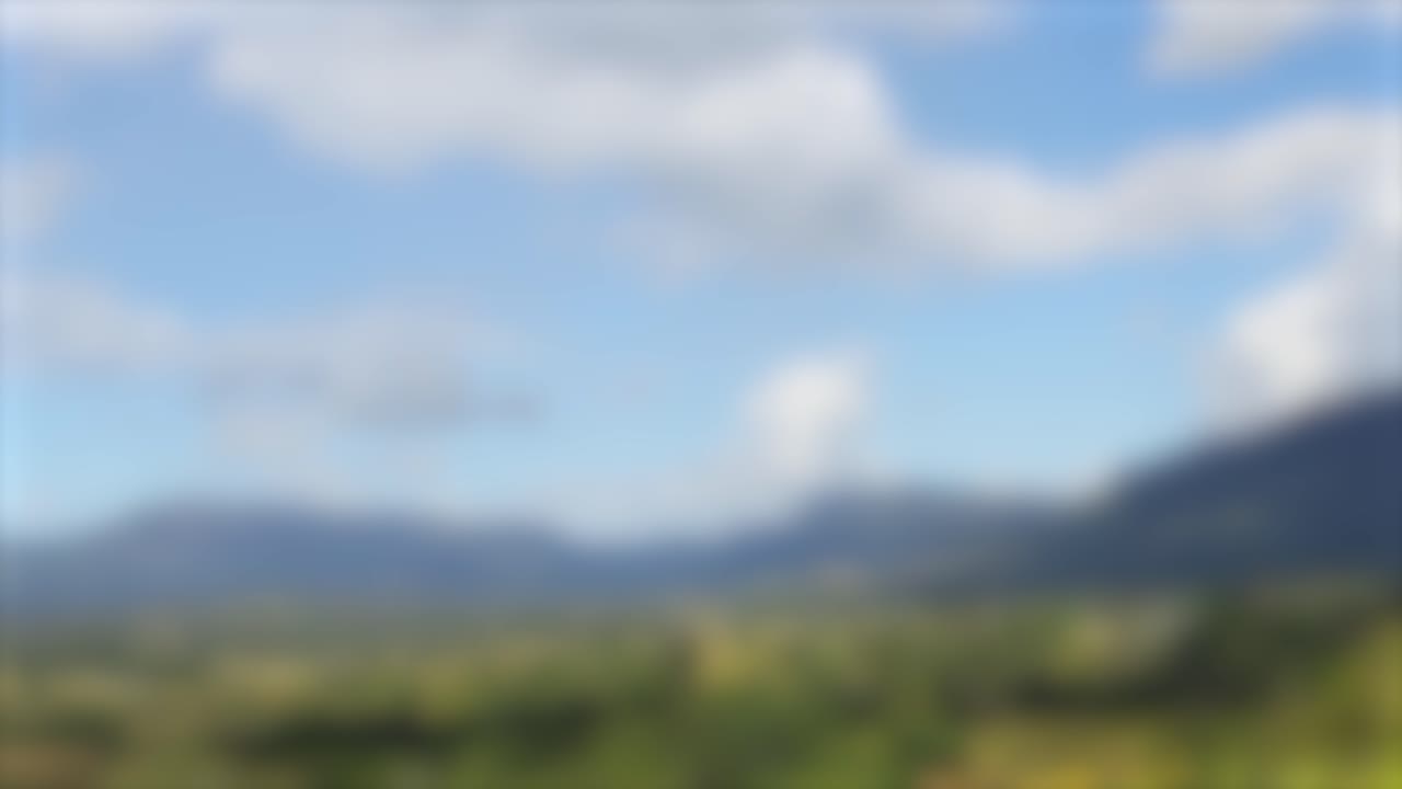 un paisaje sereno con montañas borrosas y nubes en movimiento, capturado en la suave luz del día, creando una atmósfera tranquila y soñadora