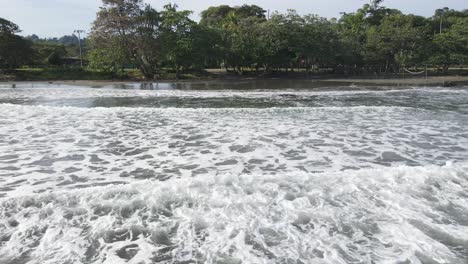 AERIAL---Camera-dolly's-back-as-waves-with-ocean-foam-push-forward-onto-shore