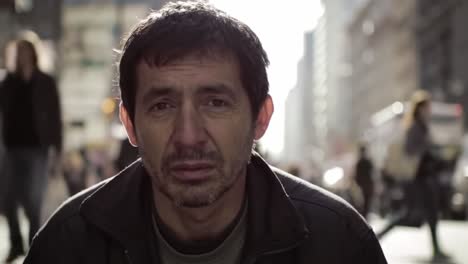 a man with a contemplative expression sits on a bustling city street, surrounded by pedestrians.