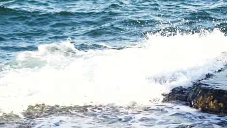 Natural view of waves breaking into dark rocks near beach. Sea waves with white foam on the dangerous stones. Ocean waves crashing against the rocks on the shore. Close-up.