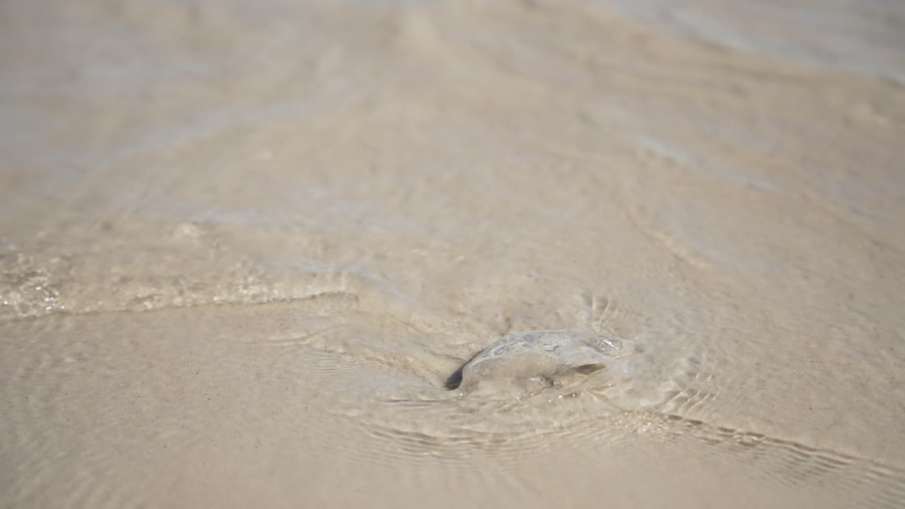 A wave crashes over a piece of plastic waste on a sandy shoreline, highlighting environmental pollution and the impact of marine debris.