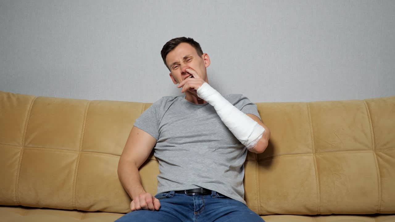 un hombre moreno pega la nariz con el brazo roto.