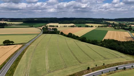aerial establishing shot of american farmsteads with green and yellow cultivated farm fields at cloudy day. growing hills in distance. wide shot. panorama. suburb highway road leading into mountains.