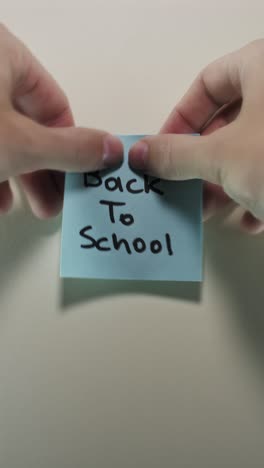 hands posting back to school sticky note on light wall, depicting the essence of learning