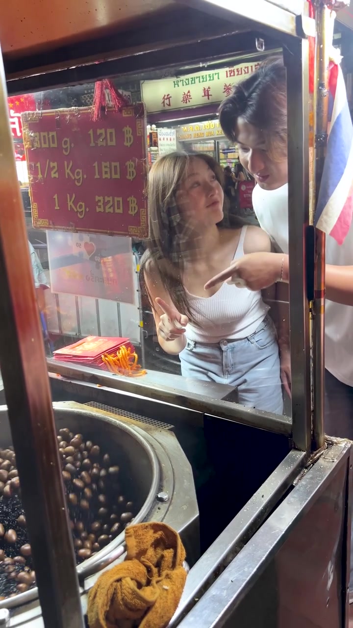Giovane coppia assaggia castagne arrostite a una vivace bancarella di cibo di un mercato notturno, illuminazione calda, momento spontaneo.