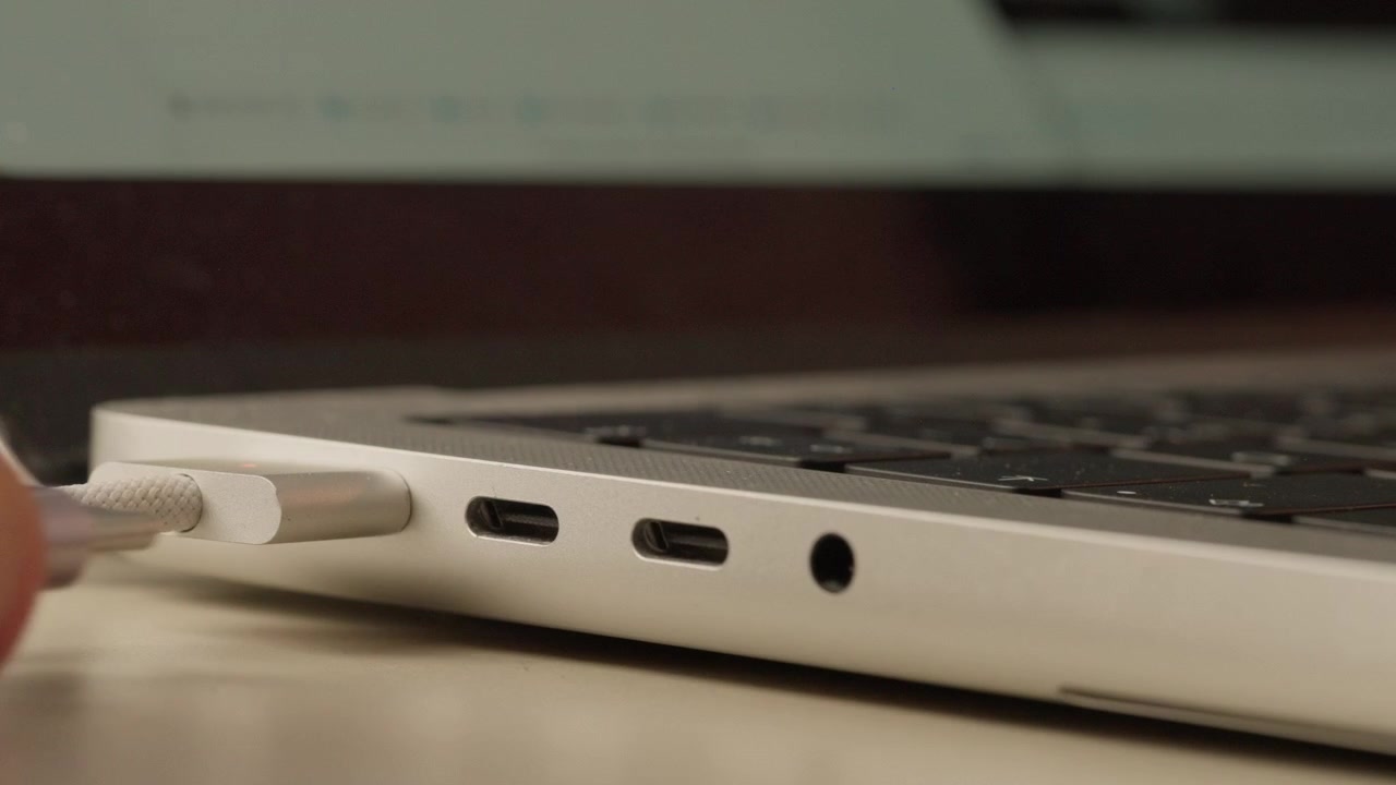 Extreme close-up of a white cable being unplugged from the USB-C port on the side of a laptop.