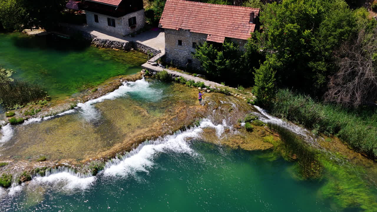 Persona che cammina su un sentiero di pietra attraverso un'acqua turchese vicino a un vecchio mulino nel fiume Mreznica in Croazia. - ripresa aerea