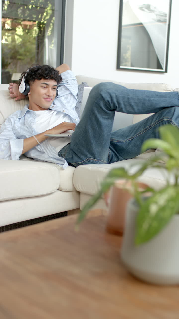 Vertical video: Relaxing on sofa, young person enjoying music with headphones at home