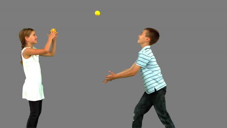 siblings playing with tennis balls on grey screen