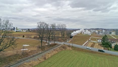 a drone view of a steam locomotive with passenger coaches approaching with a full head of steam over countryside on a winter day