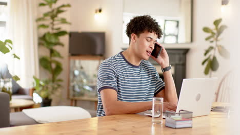 Biracial-Mann,-Der-Von-Zu-Hause-Aus-Mit-Laptop-Arbeitet-Und-Auf-Dem-Smartphone-Spricht,-Zeitlupe