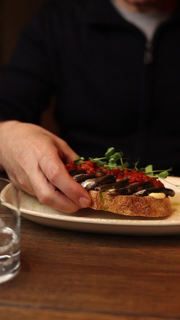 persona comiendo una tostada de anchoa y tomate