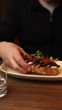 person eating an anchovy and tomato toast