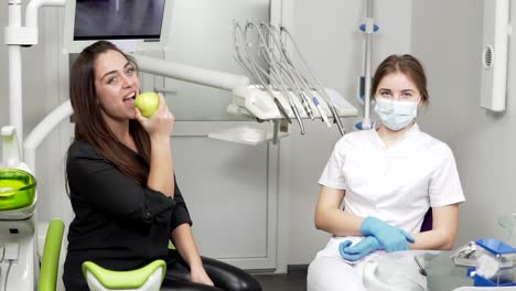 in the dental office girl biting a green apple sitting near the dentist after the procedures. healthy teeth and healthy smile