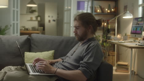 man typing on laptop on sofa at home