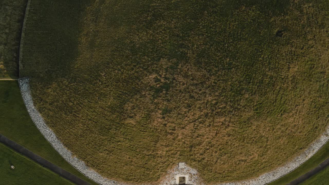 Ancient grass-covered mound with circular patterns in Ireland seen from above during sunrise