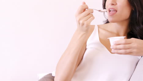 Woman-sitting-on-a-sofa-eating-a-yoghurt