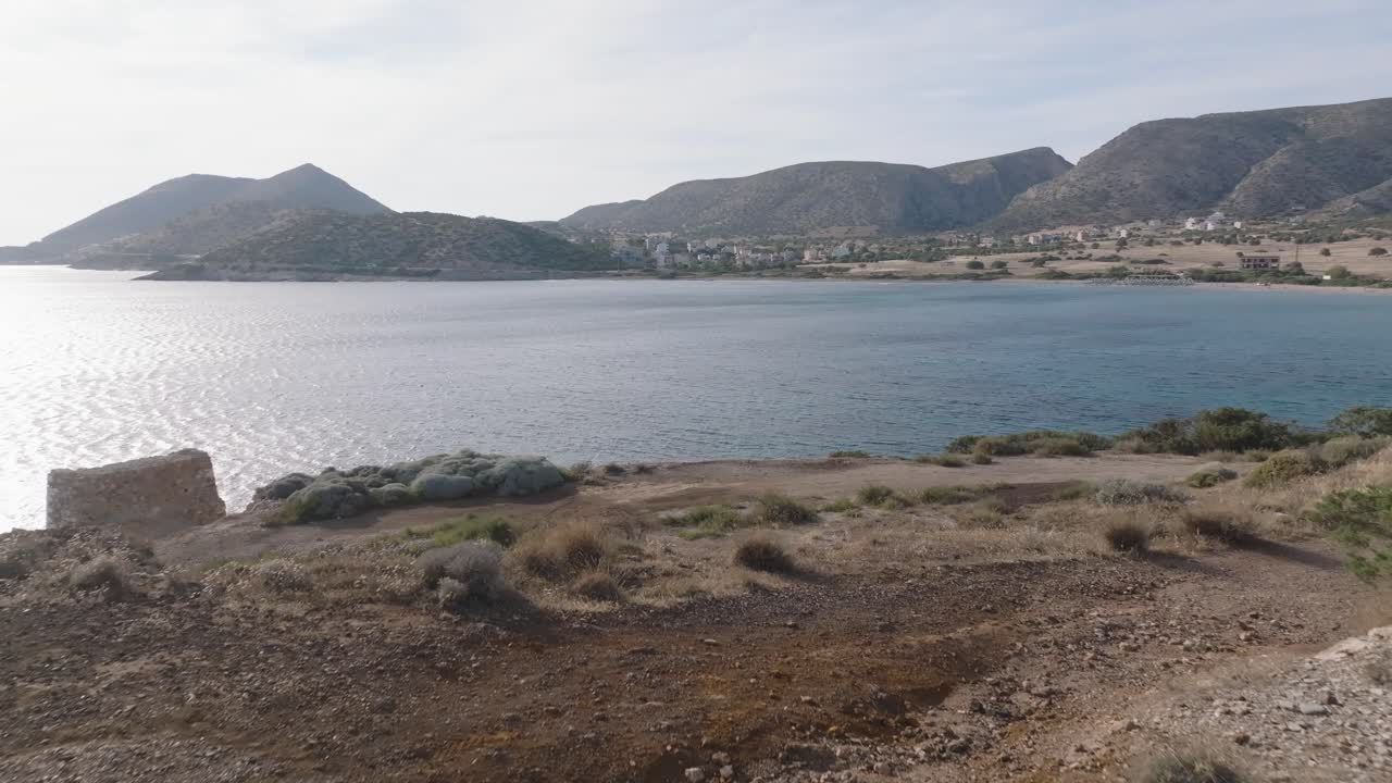 Woman walking to edge of bay and enjoying beautiful coastline view in Greece at sunset - Aerial forward flight