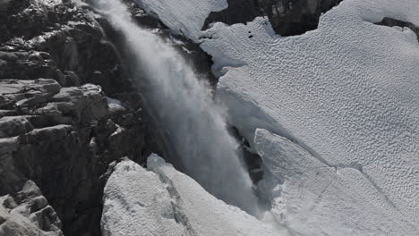 slowmotion drone shot flying around a powerfull waterfall near langvatnet lake in norway close to the strynefjellsveg breaking through ice and snow on a sunny day surrounded by shiny rocks log