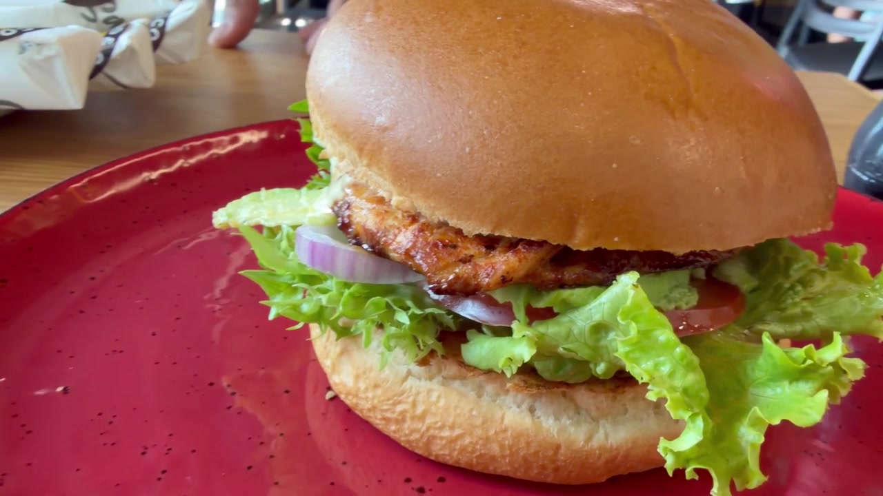 Un hamburger di pollo su un piatto rosso con lattuga, pollo e salse