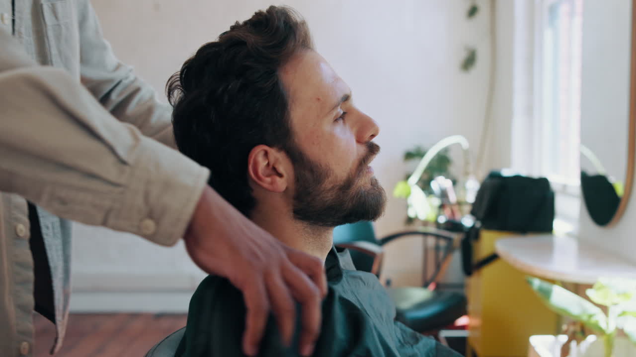 Barber tager beskyttende kappe på mandlig kunde i salon