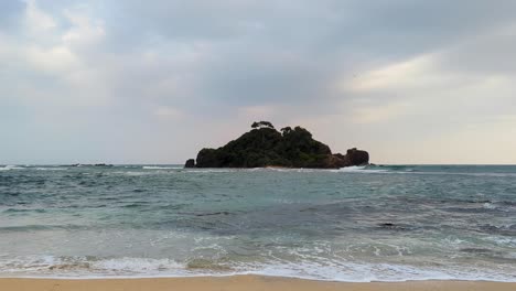 scenic view of devil's rock island, ocean, and waves with birds flying at dusk in midigama, south coast sri lanka