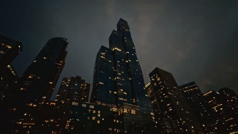 a cinematic low-angle shot of illuminated skyscrapers in downtown chicago during twilight. the city lights reflect off the glass windows as dusk settles in.