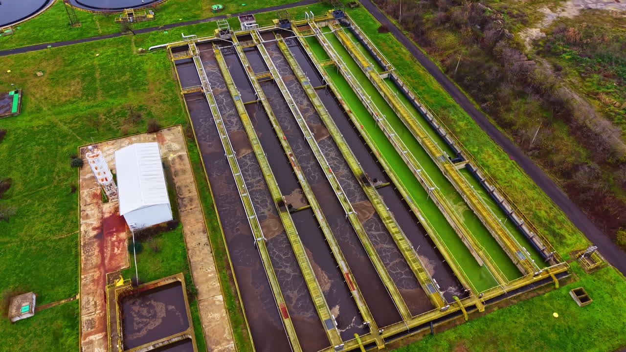 Wastewater treatment facility viewed from above during daytime showing numerous tank structures and green spaces surrounding the area