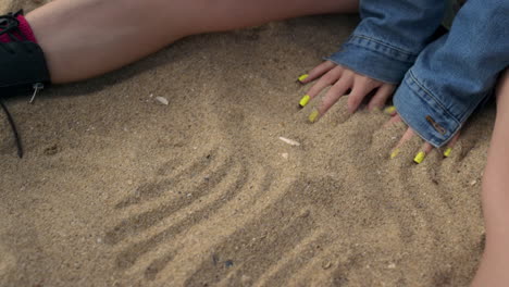 Manos-De-Niña-Desconocida-Dibujando-Líneas-En-La-Arena-De-La-Playa-De-Cerca.-Señora-Disfruta-De-La-Naturaleza.