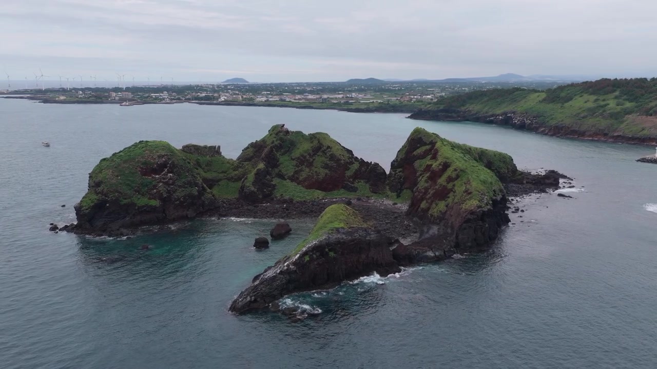 Vista aérea horizontal de los islotes de Chagwido cerca del Sendero Costero Eongal en la Isla de Jeju, Corea del Sur, con la cámara avanzando mientras se desplaza a la izquierda sobre los islotes volcánicos y el mar circundante